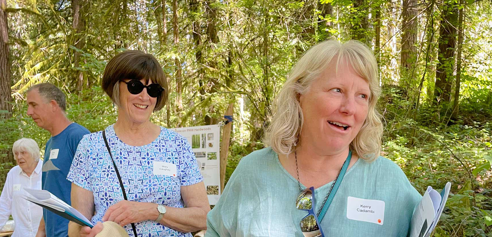 A group of people with nametags and brochures walking through a wooded area during a forest landowner event.