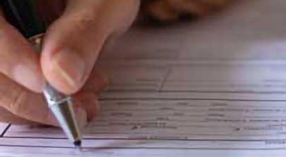 A hand holding a pen and filling out a printed form on a table.