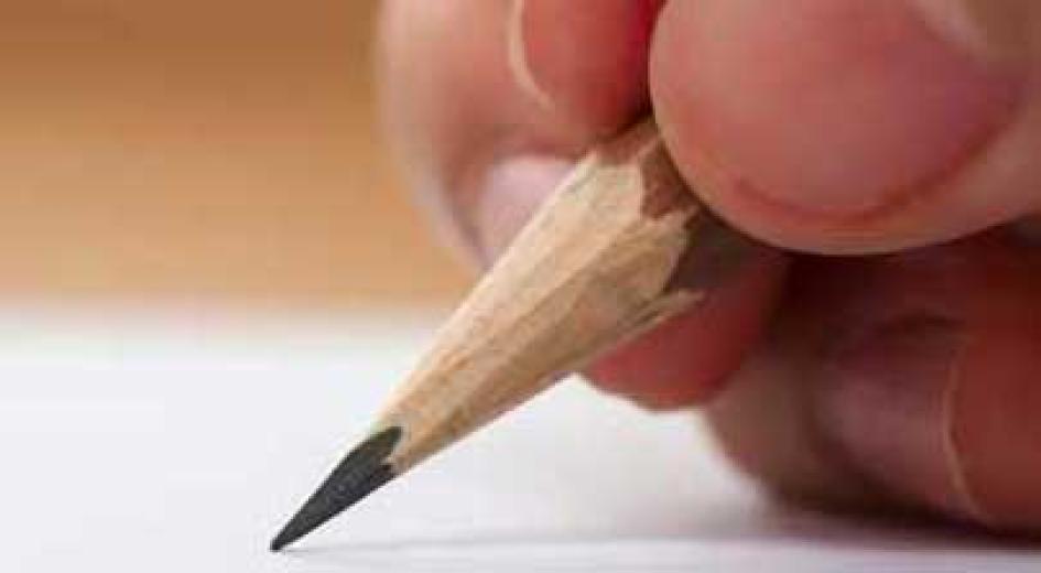 Close-up of a hand writing with a sharpened pencil on white paper.